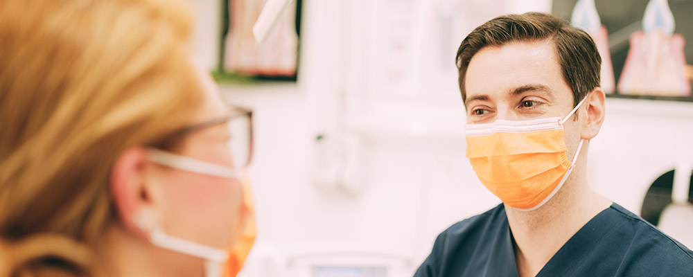 Zahnarzt mit Mundschutz lächelt nach einer erfolgreichen Füllungstherapie in Berlin-Spandau. 